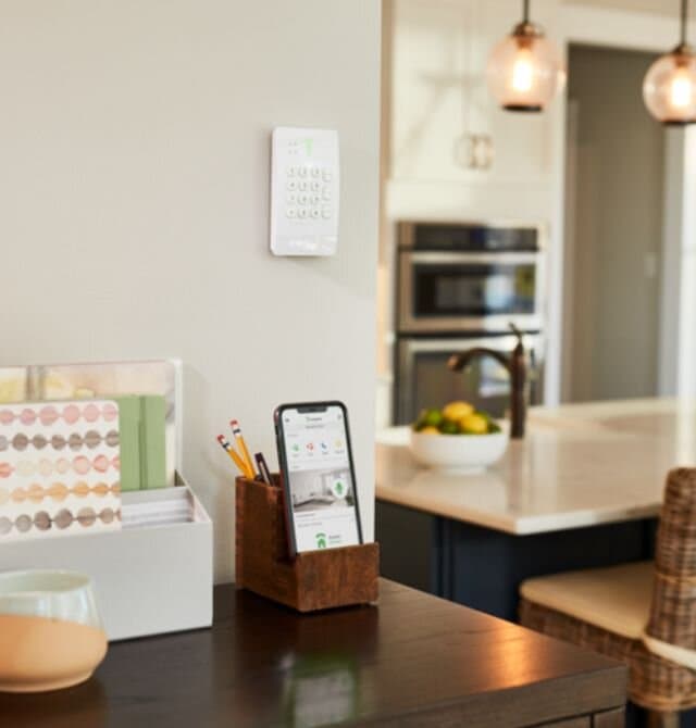 Frontpoint security keypad on a kitchen wall with the mobile app nearby